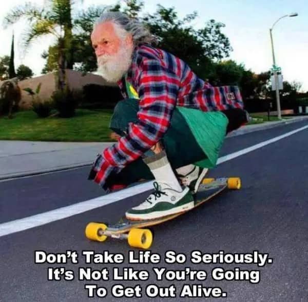 Bearded older man in a flannel shirt crouched on a longboard, speeding down a street.