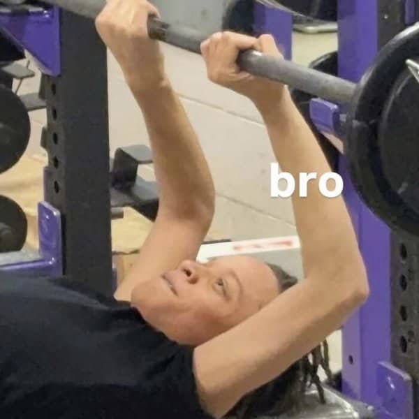 Woman lying on a gym bench gripping a barbell awkwardly overhead with a bro caption.
