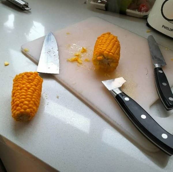 Corn cob pieces on a cutting board surrounded by several large kitchen knives.