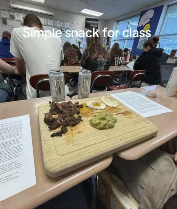 Steak, fried eggs, guacamole, and energy drinks on a cutting board on a classroom desk.