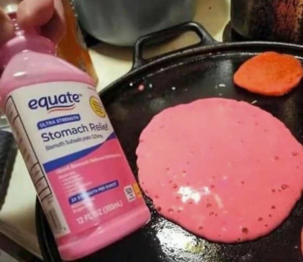 Pink pancake batter cooking on a griddle beside a bottle of stomach relief medicine.