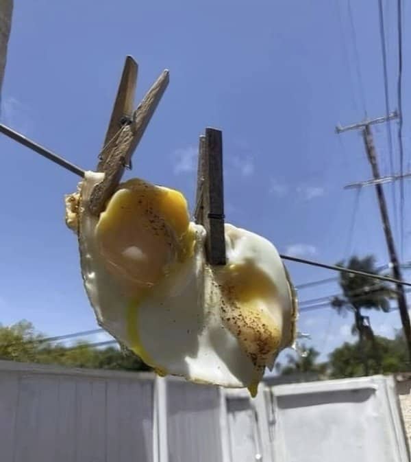 Two fried eggs hanging on a clothesline with wooden clothespins under a sunny sky.