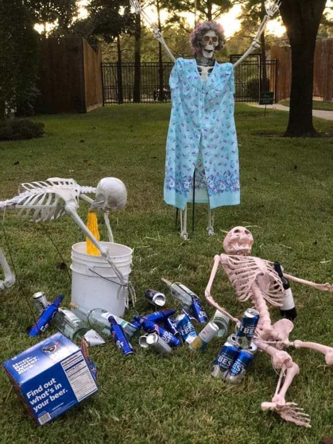 Halloween skeleton yard display with a party scene, beer cans, and one skeleton getting sick.