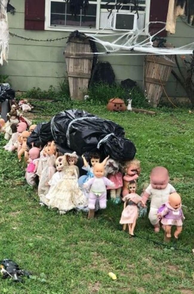 Yard covered with old dolls lined up around black trash bags beside wooden coffins.
