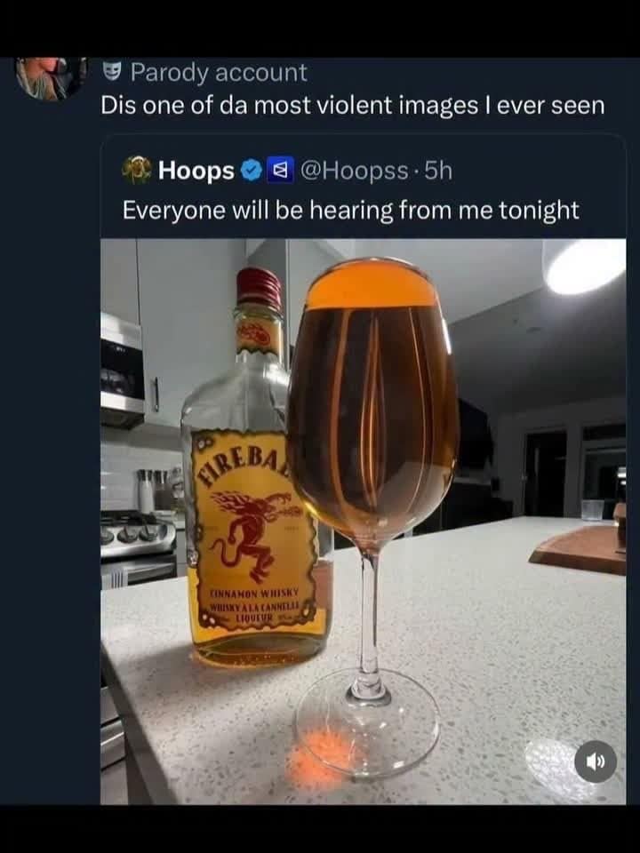 Wine glass filled to the brim with cinnamon whisky beside the bottle on a counter.