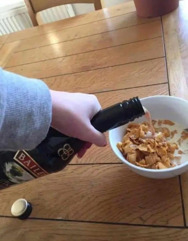 Hand pouring a bottle of Baileys over a bowl of cornflakes instead of milk.