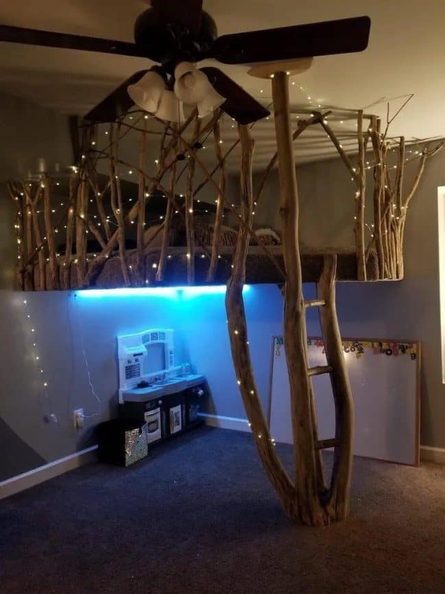 Kids loft bed built from real tree branches with fairy lights and a play kitchen underneath