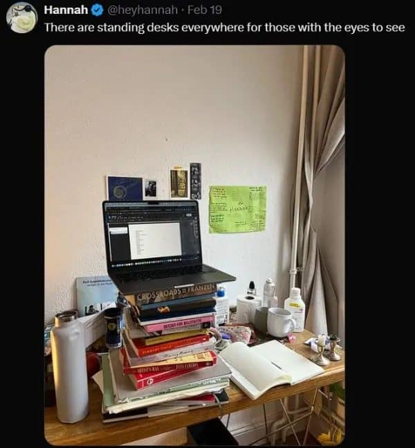 Laptop balanced on a tall stack of books, posted as a homemade standing desk.