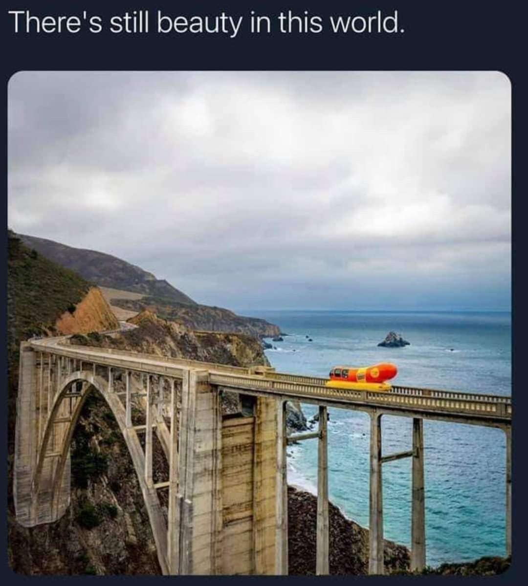 The Oscar Mayer Wienermobile crossing a scenic coastal arch bridge beside the ocean.