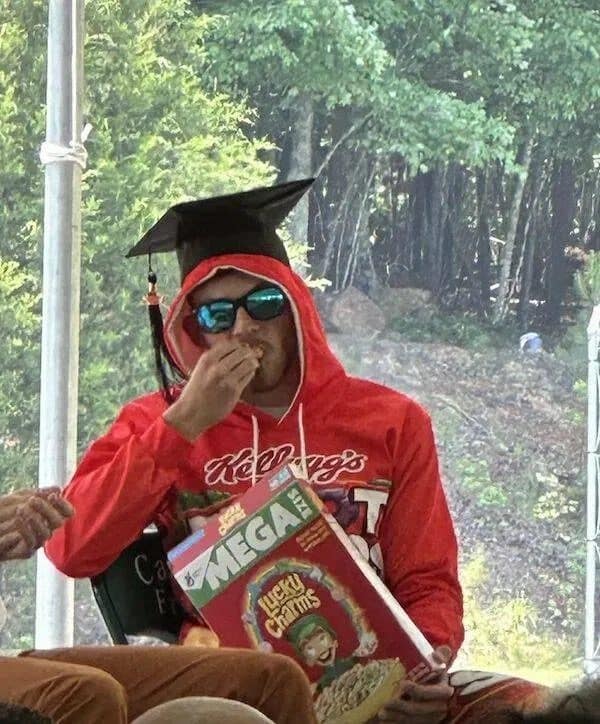 Graduate in a cap and red Kellogg's hoodie eating from a giant box of Lucky Charms.