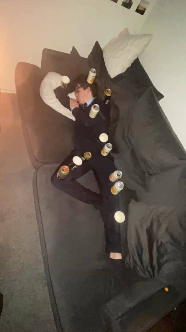 Young man in a suit asleep on a couch, decorated with beer cans and ping pong balls.