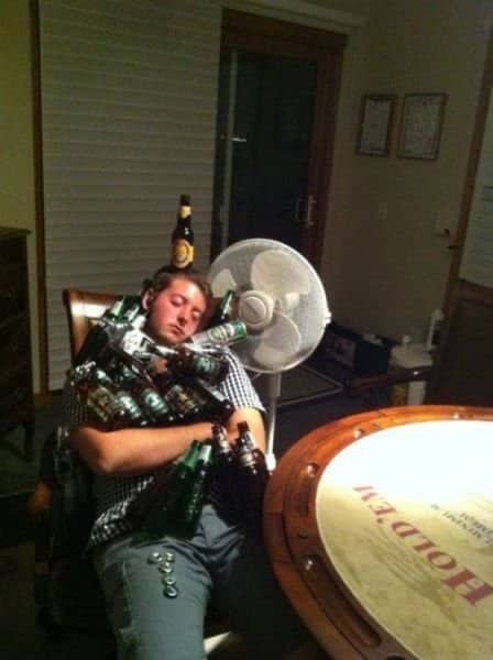 Young man asleep in a chair hugging an armful of beer bottles with one balanced on his head.