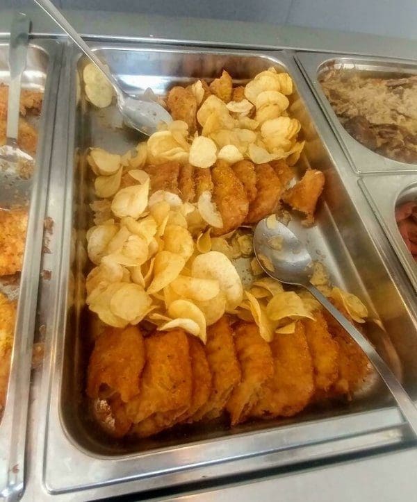 Buffet tray of fried fish fillets with a pile of potato chips dumped on top.