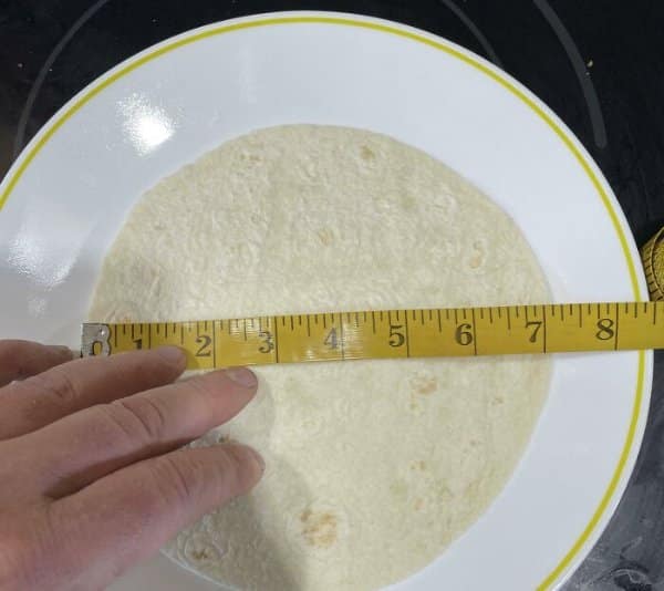 Tape measure across a tortilla that falls short of its advertised size.