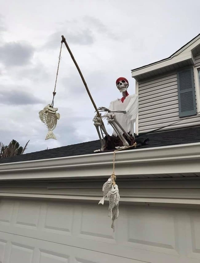 Pirate skeleton fishing from a garage roof with a line of fish skeletons hanging below.
