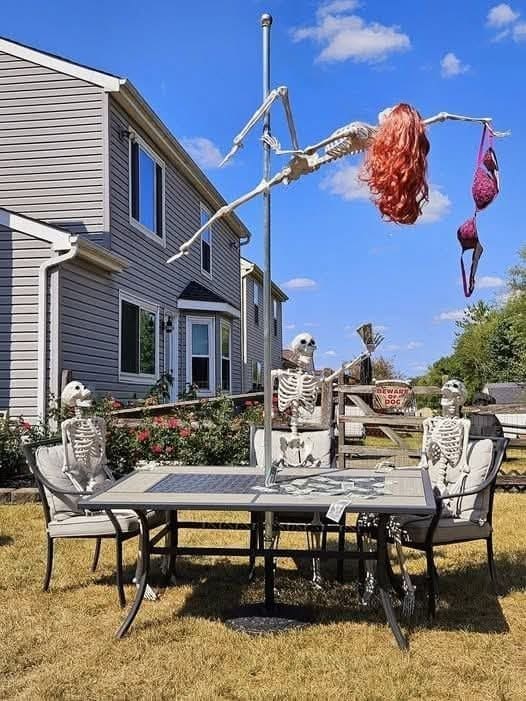Backyard skeleton display with a red-wigged skeleton on a pole above skeletons at a table.
