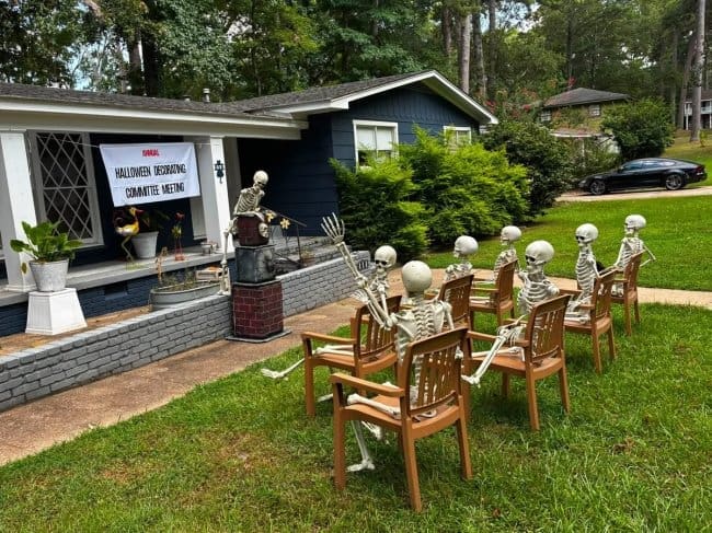 Skeletons seated in rows of chairs at an annual Halloween decorating committee meeting.