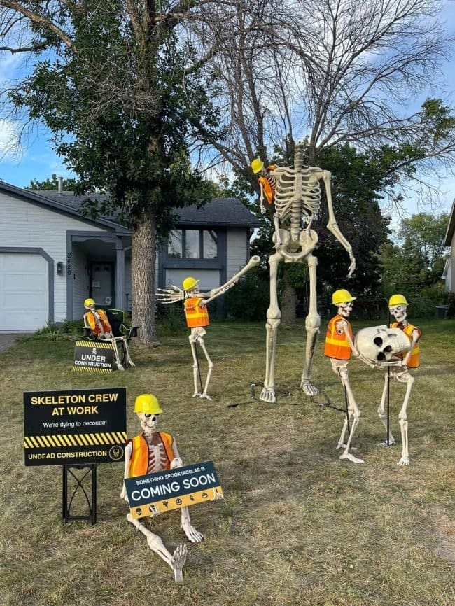 Skeletons in hard hats and safety vests building a giant skeleton under construction.