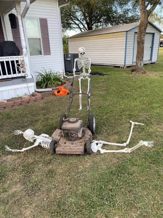 Skeleton pushing a lawn mower over another skeleton's scattered bones in a front yard.