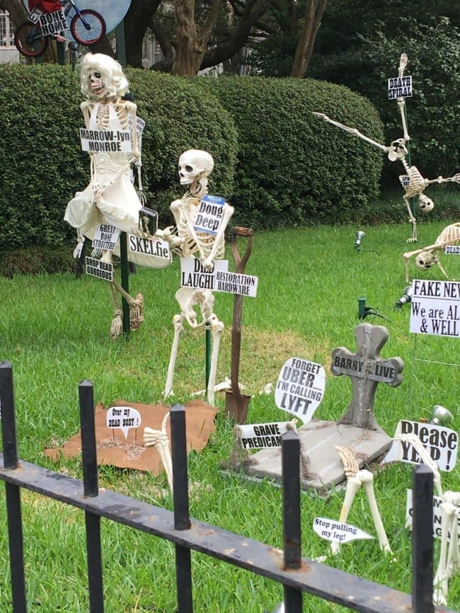 Front yard full of skeleton memes with pun signs like Marrow-lyn Monroe and Doug Deep.