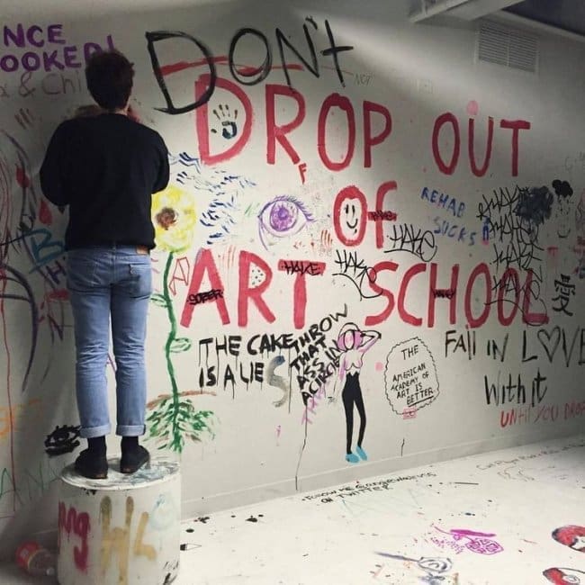 Student painting a crowded wall that reads don't drop out of art school.