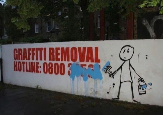 Graffiti removal hotline sign painted over by a stick figure holding a paintbrush.