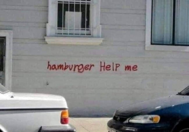 Red graffiti on a white house wall reading hamburger help me.