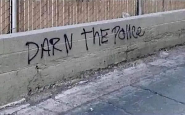 Graffiti on a low concrete wall reading darn the police in shaky letters.