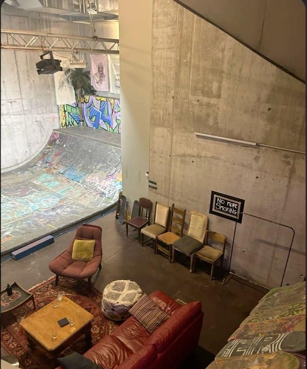 Living room with sofas, rugs and mismatched chairs built right beside a graffiti-covered skate bowl.