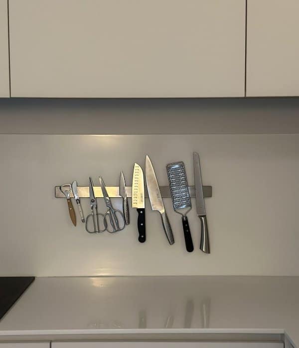A magnetic strip under kitchen cabinets holding knives, scissors, a peeler and a cheese grater.