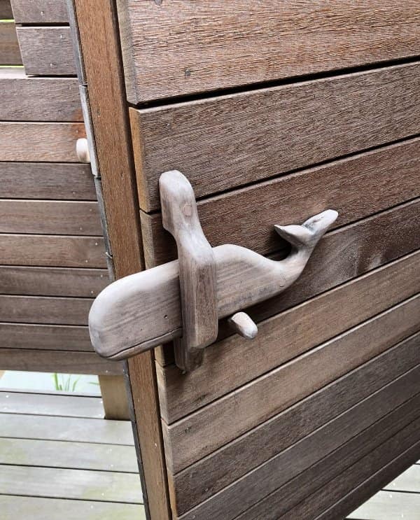 A wooden gate latch carved into the shape of a whale, sliding through a wooden bracket.