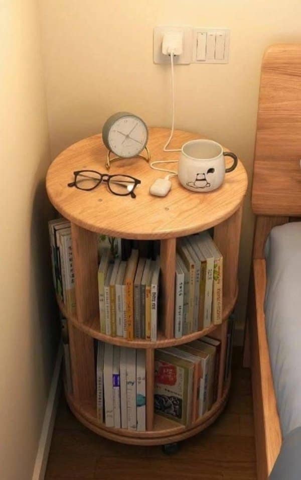 Small rotating bookshelf nightstand holding a clock, glasses and mug, one of the unique designs for bedrooms.