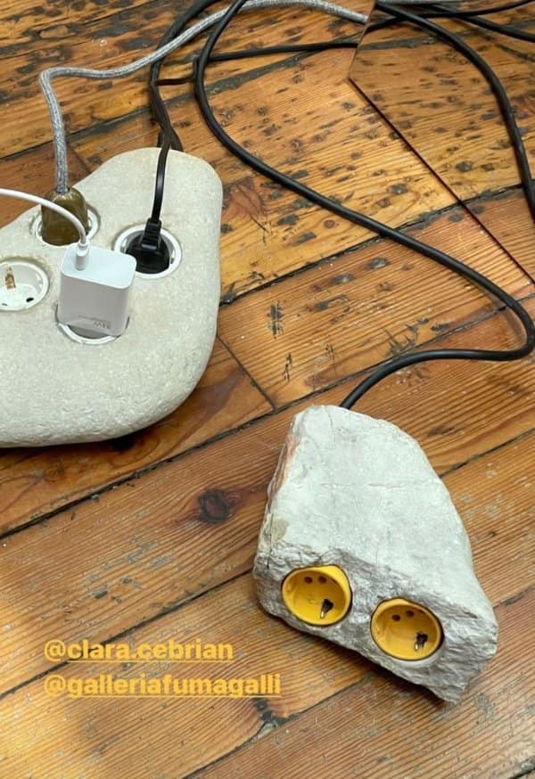 Two power strips carved into rough stones, plugged in and sitting on a worn wooden floor.