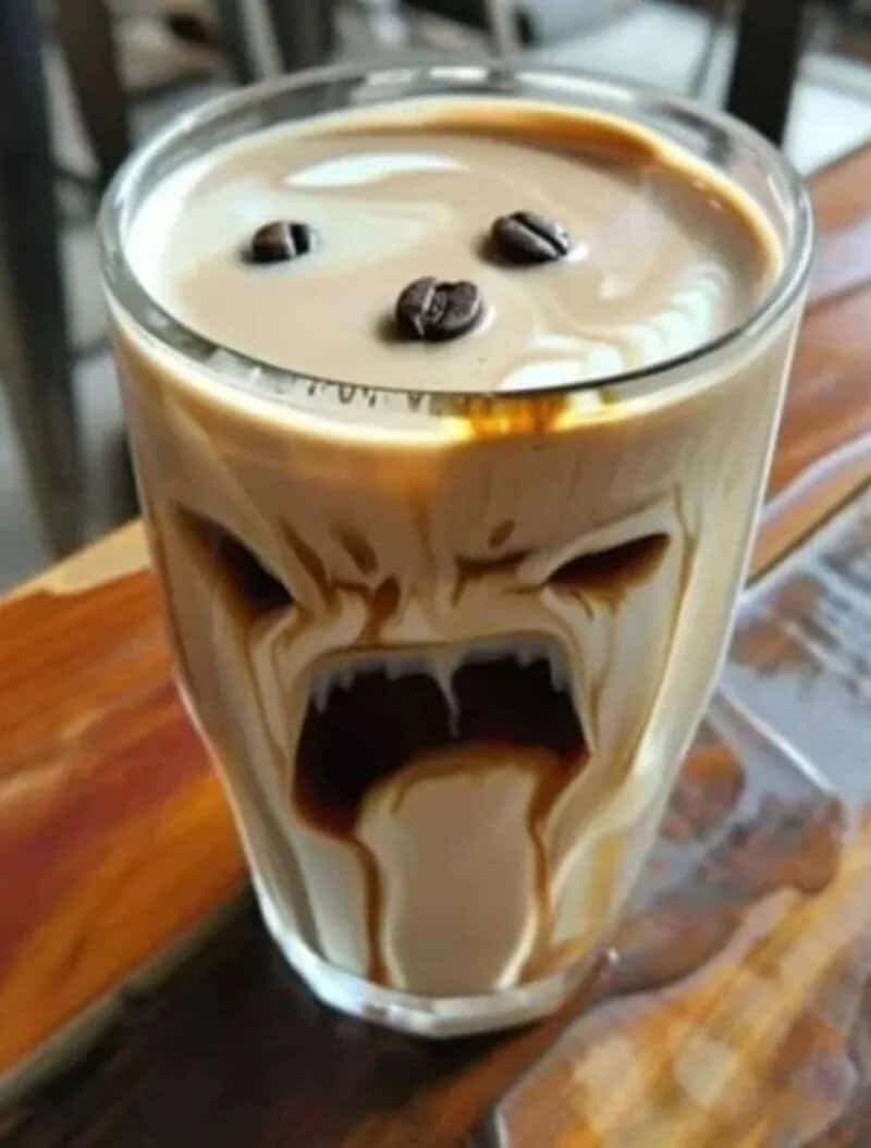 Glass of iced coffee where swirls of espresso form a screaming face.
