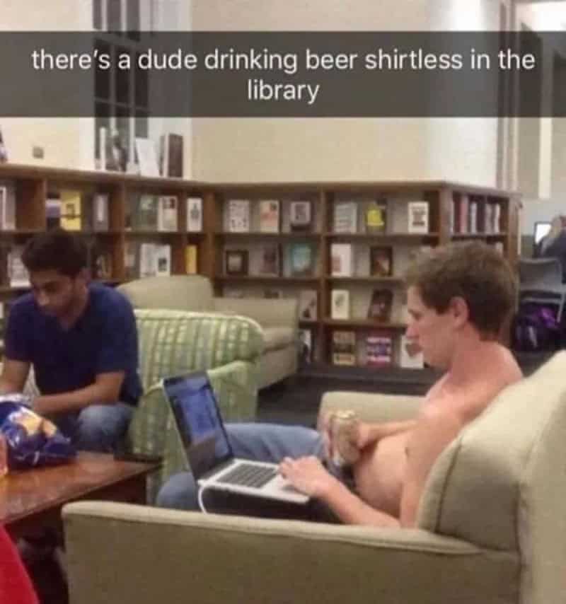 Shirtless guy drinking a beer on his laptop in a campus library lounge.