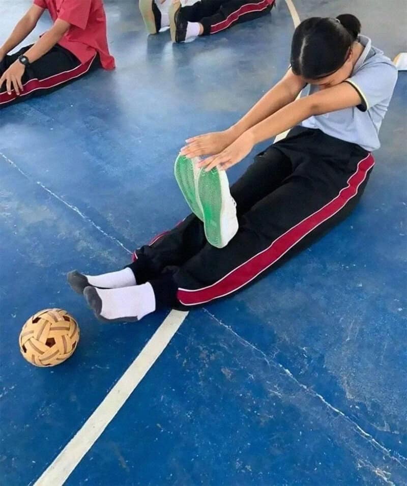 Student doing a seated stretch by holding her shoes instead of reaching her feet.