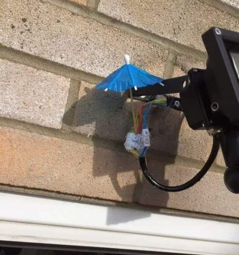 Tiny cocktail umbrella stuck above exposed wiring connectors under an outdoor light.