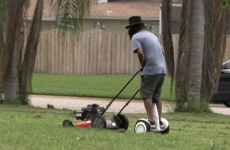 Man mowing his lawn while standing on a self balancing scooter.