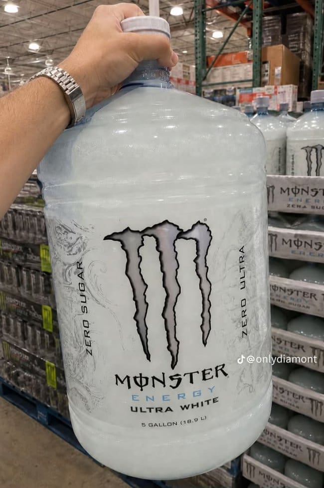 Hand gripping a five gallon jug of Monster Ultra White in a warehouse store.