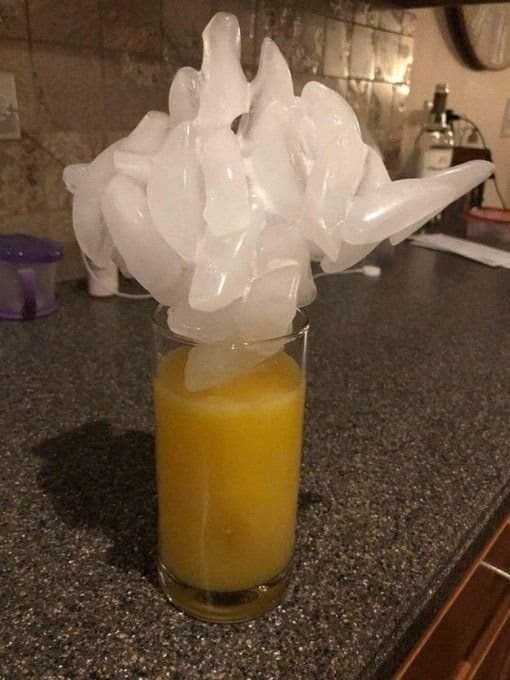 Glass of orange juice crowned with a huge, towering cluster of ice on a counter.