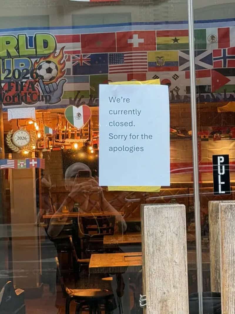 Restaurant door sign reading we're currently closed, sorry for the apologies, under World Cup flags.