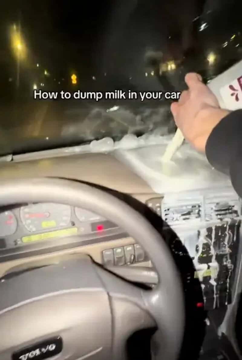 Person pouring a jug of milk across a car dashboard and into the air vents at night.