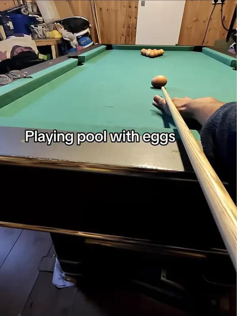 Pool table racked with brown eggs while someone lines up a shot at a cue egg.