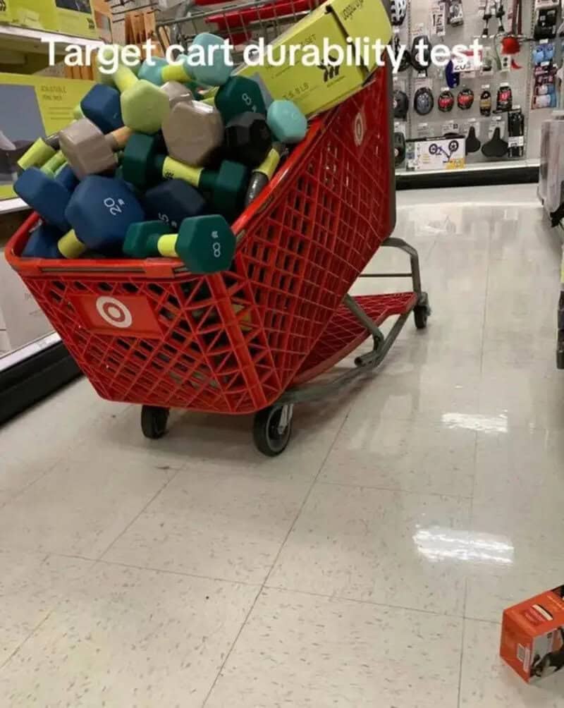 Red Target shopping cart buckling under a heavy pile of colorful dumbbells in the aisle.