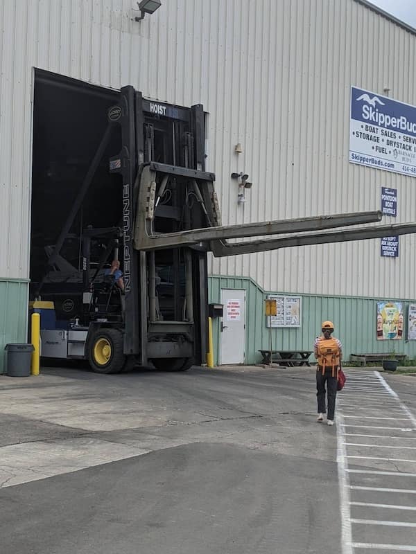 A massive forklift extending far out of a warehouse entrance, dwarfing a pedestrian nearby.