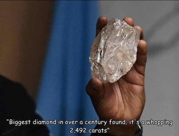 A hand holding a massive, uncut diamond with a caption about its record-breaking carat size.