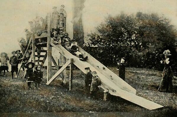 A vintage photo of a very tall and extremely steep wooden slide from a dangerous old-fashioned public playground.