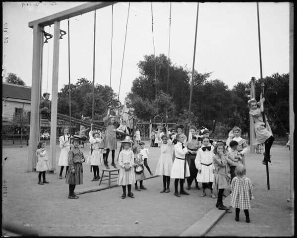 A vintage photo of a dangerous playground with very high swings and climbing poles over the hard ground.