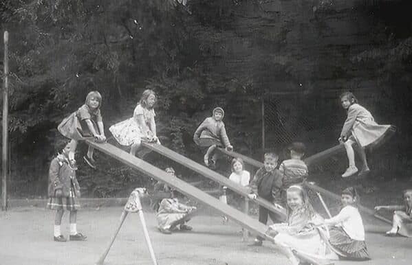 A vintage photo from a dangerous playground of kids flying high up in the air on old-fashioned metal seesaws.