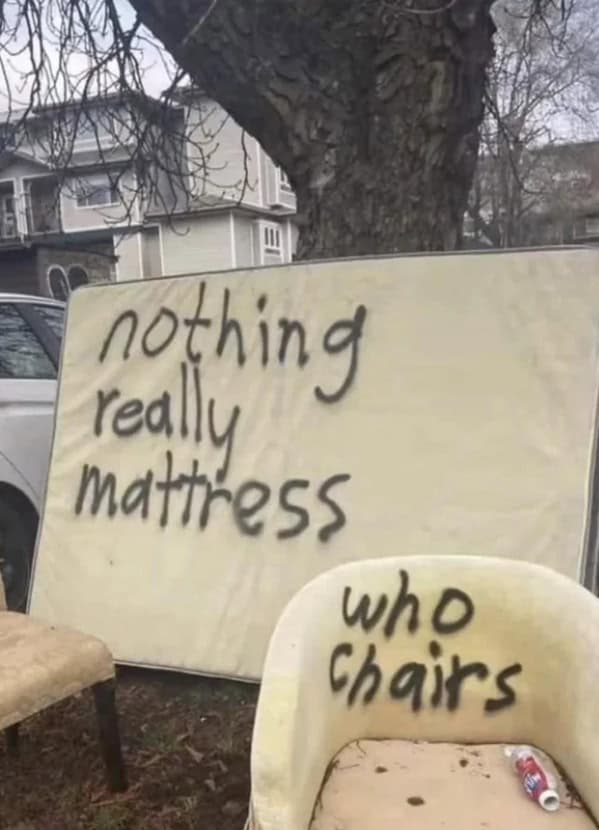 Old mattress spray-painted “nothing really mattress” beside a chair tagged “who chairs.”